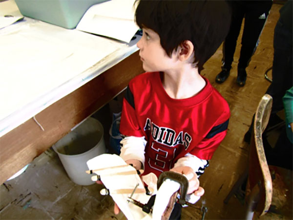 AJ is ready for the dye. He has tightly wrapped popsicle sticks on his material and used a vise to hold a pair of wood cutouts.