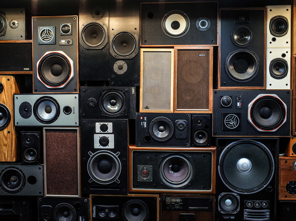 a wall of various audio speakers all stacked together, with the woofers and the tweeters visible.