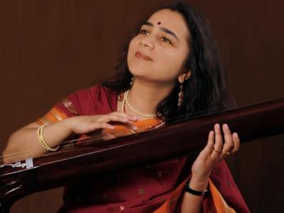 Srivani Jade holding a long Indian string instrument, looking up with a calm, blissful expression
