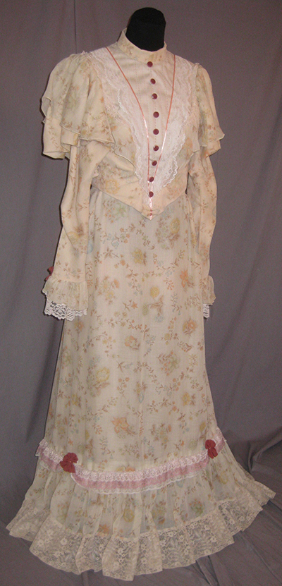 light colored dress of diaphonous floral fabric. Red accents, buttons, etc., lace at the hem and sleeves