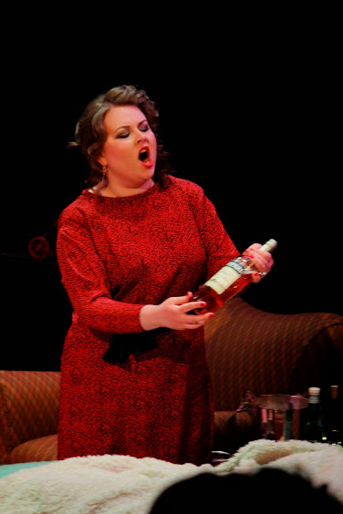An actor sings meaningfully to a bottle of red fluid.