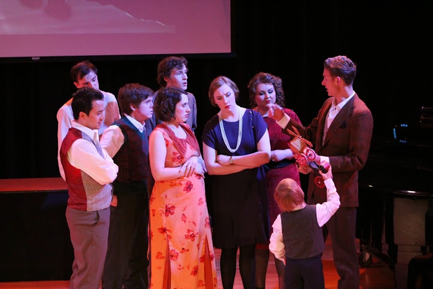 group of actors in semi formal dress sing to each other. A child looks on.