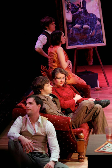 several actors, seated looking bored. Painting of rider on horse in background.