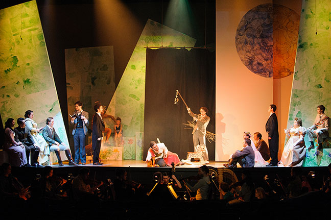 large group scene of stage. Actors seating and standing. Geometrically abstract scenery.