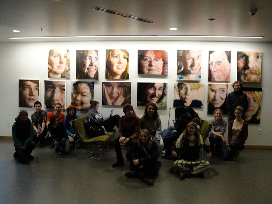 Happy people sitting for the camera in front of a series of close-up portrait paintings