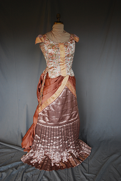 Silk dress, fitted bodice, cap sleeve, bustle. Ornate fabric and tailoring.
