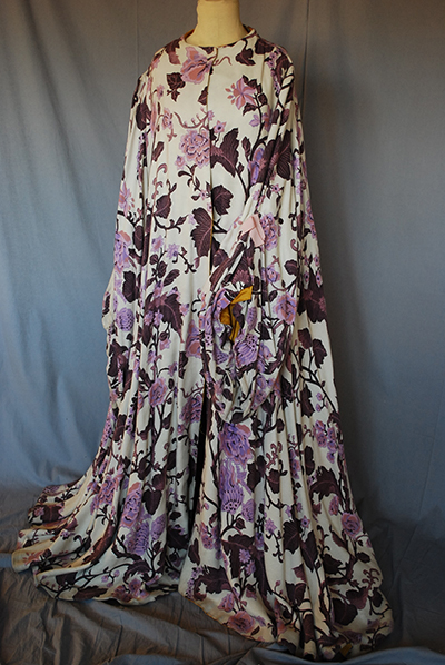 very long gown with dragging hem and sleeves. White background, heavily decorated with lavender, purple floral pattern