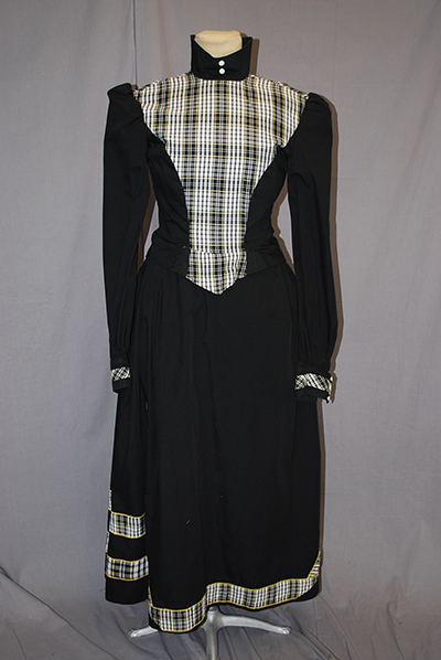 high collared bodice, long fitted sleeve, plaid plastron front at breast, black skirt with matching plaid hem.