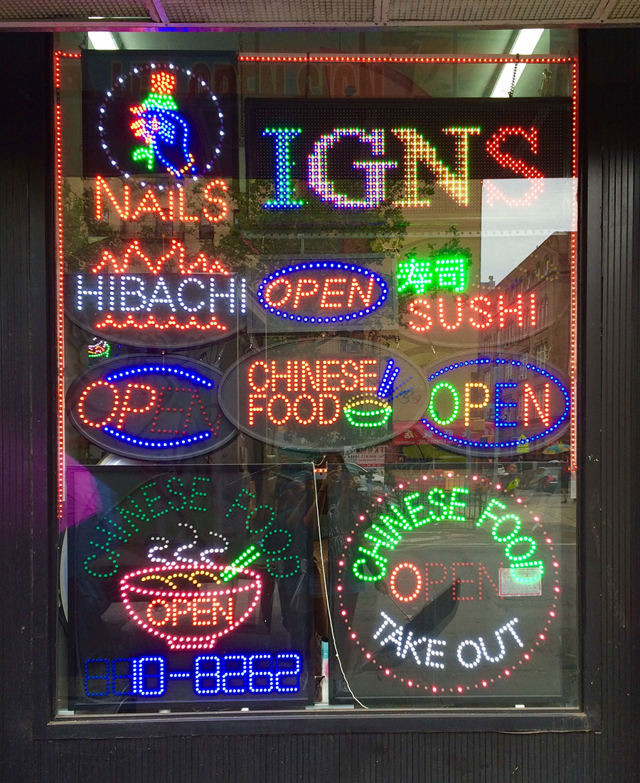 colorful window of a sign shop with many different signs advertising &quot;nails&quot; &quot;hibachi&quot; etc