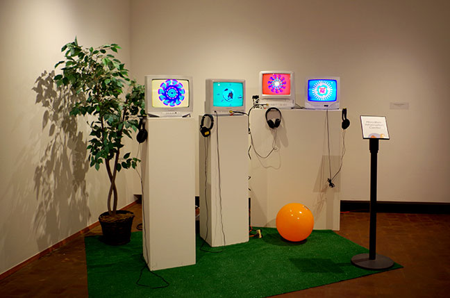 Four brightly colored video screens on pedestals. Screens are small, CRT type.