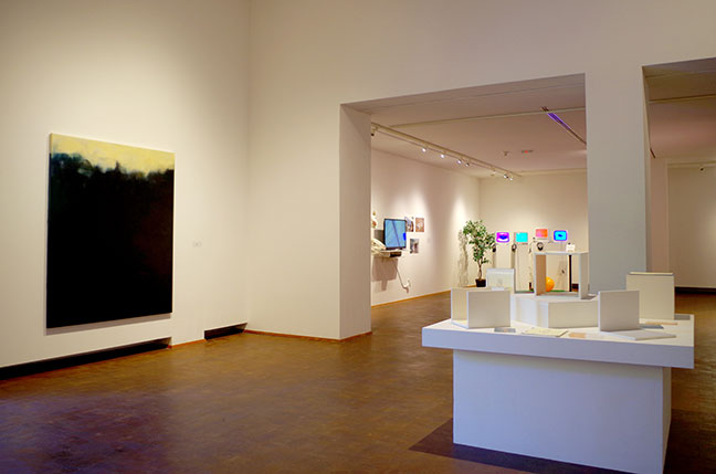 Paintings and a vitrine with sculpture in a gallery.
