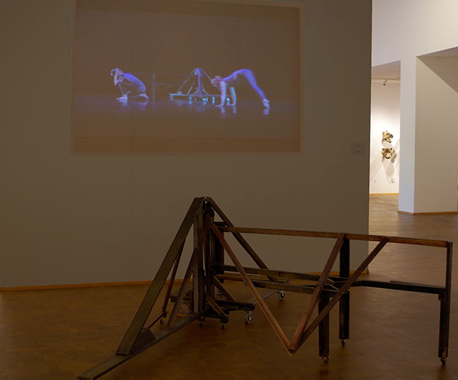 A projection of a dance work with a small structure in the foreground on the floor.