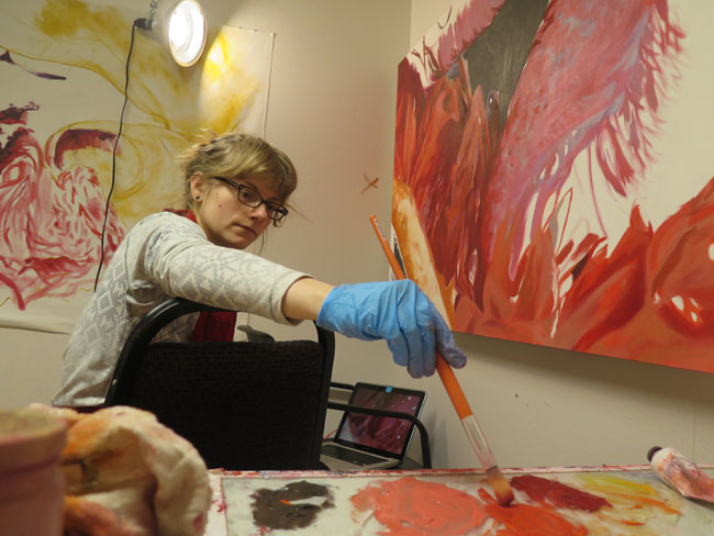 blond artist with glasses works on a large canvas