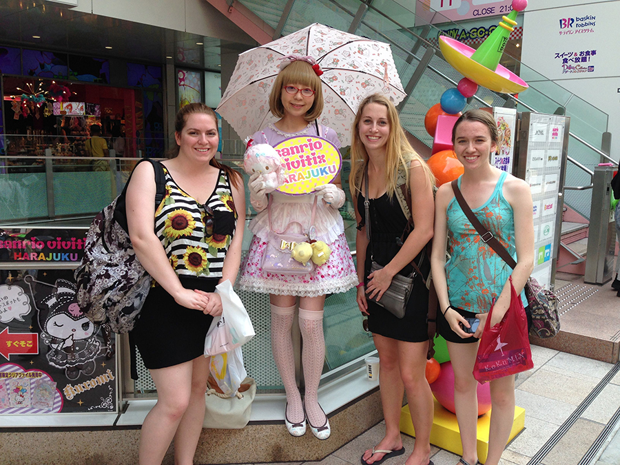 three students pose with a person in a frilly pink dress holding a parasol
