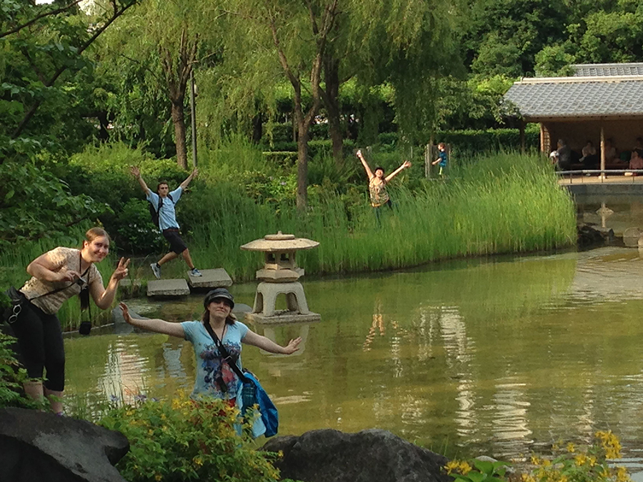 students pose around a pond in a garden amidst simple framed structures