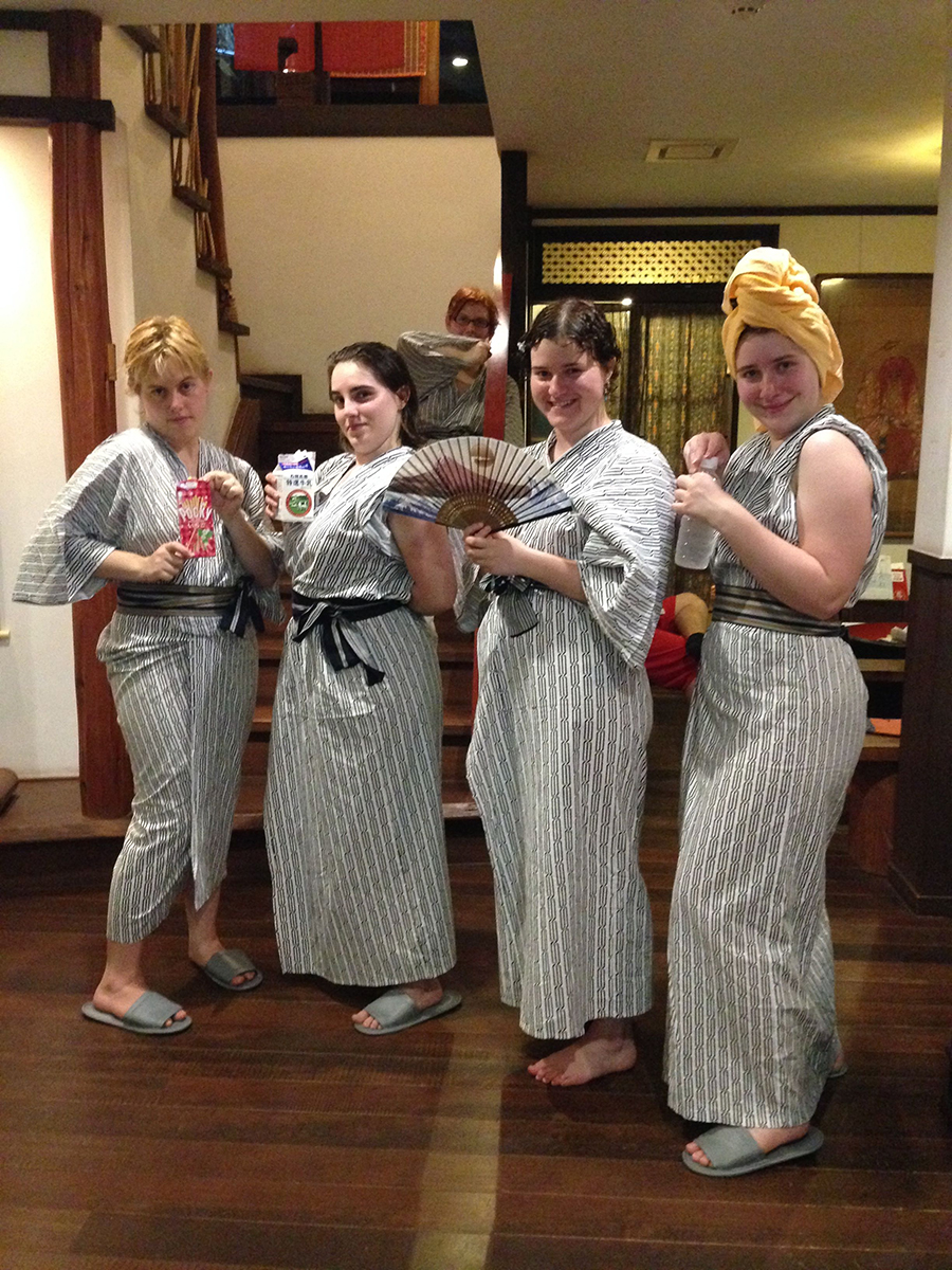 four students pose in simple kimono, each holding a beverage