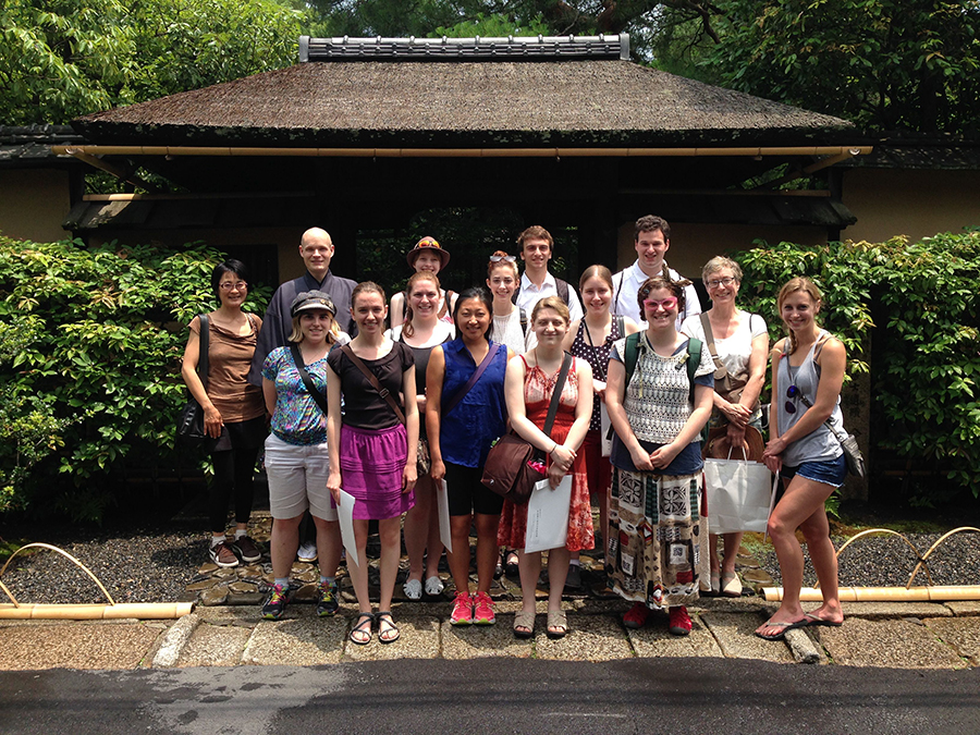 a group of students pose in front of a wooden Japanese building
