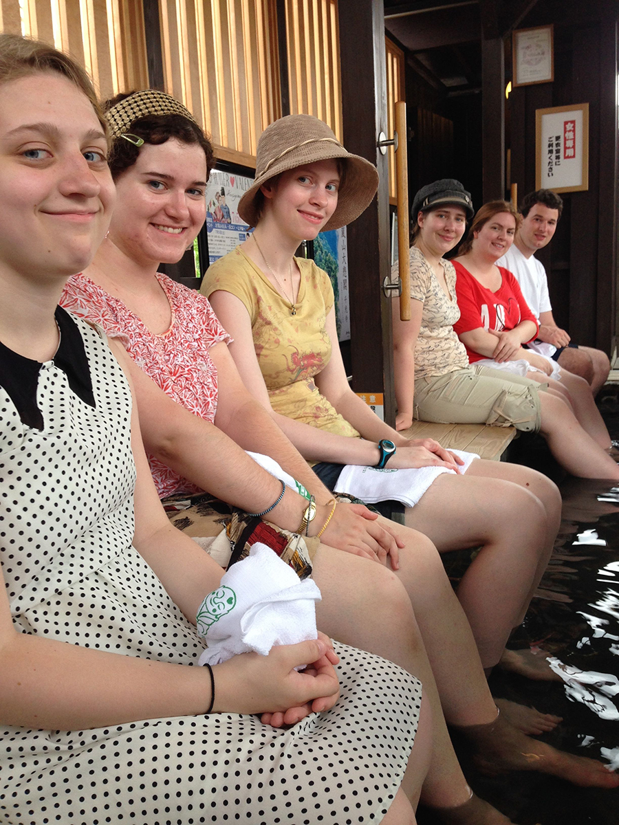 six students wait on a bench, smiling at the camera