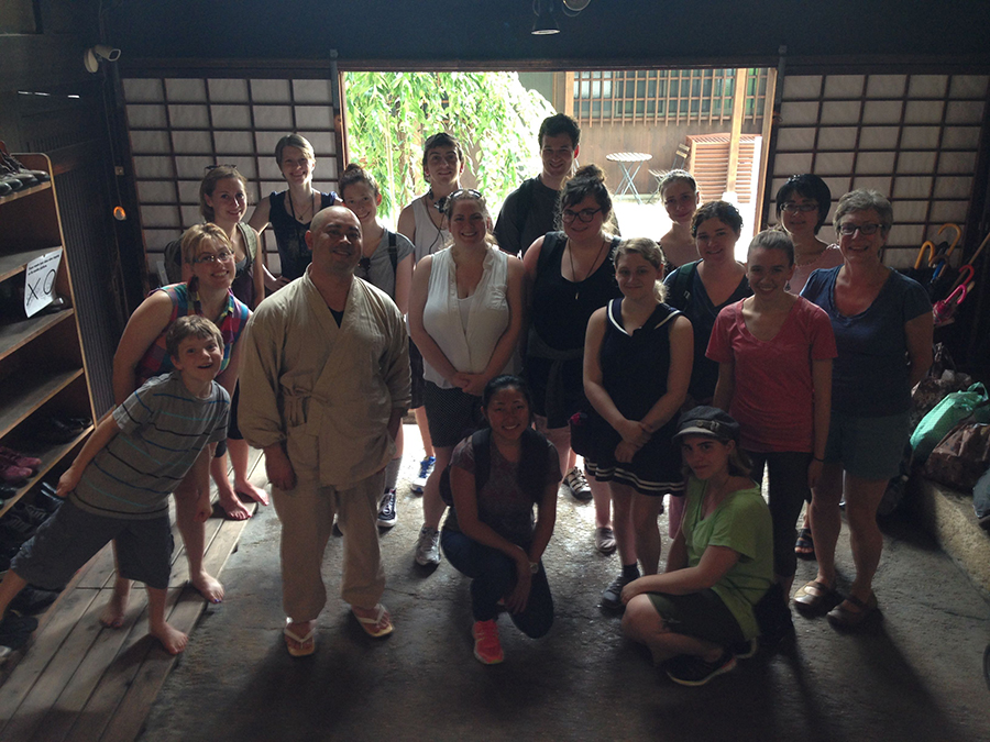 group of students pose for the camera in a shady room with rice paper dividers in the background.