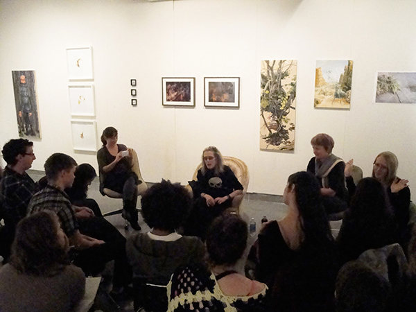 People seated in a circle, engaged in discussion. The wall behind them is filled with 2D art