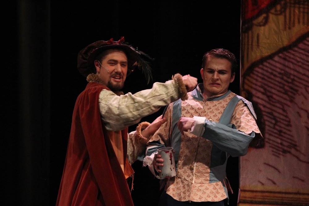 A dashing actor in a feathered hat annoys another actor in a doublet