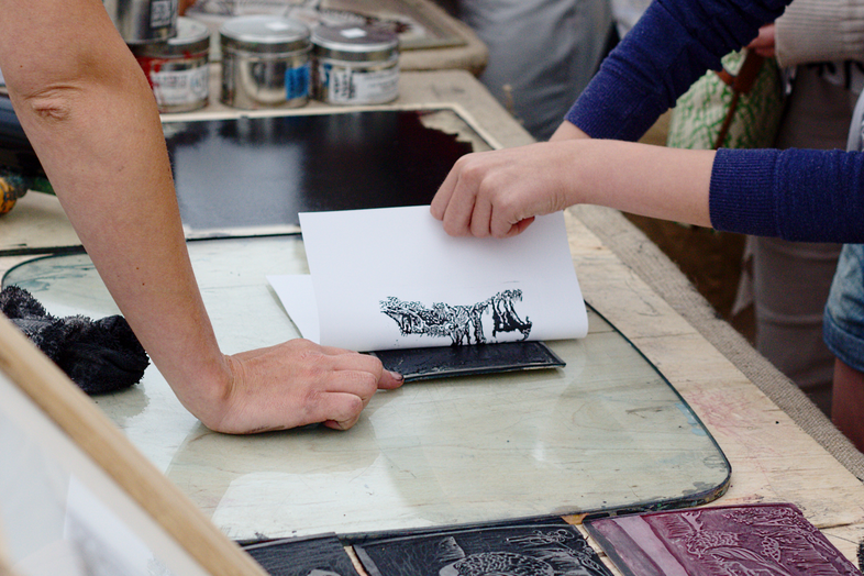 printmaking students peel a print off a cut block in the print lab