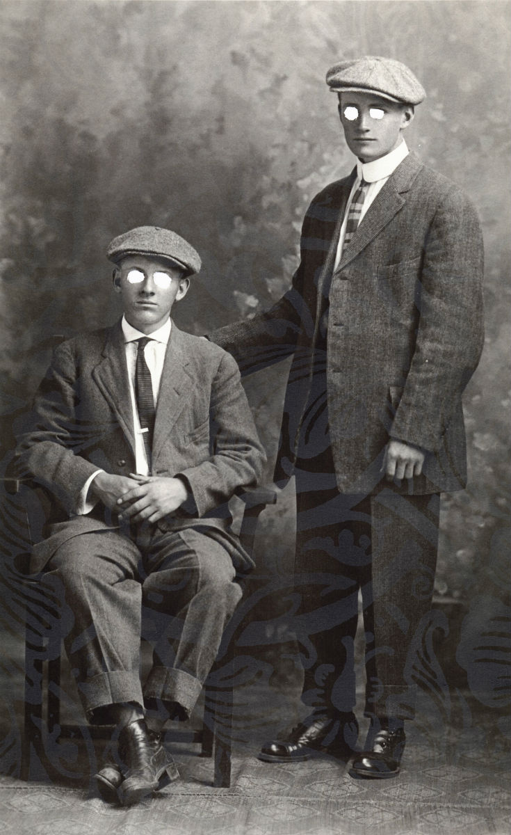 vintage photo, one man seated, one standing. The image has holes where the eyes normally go.