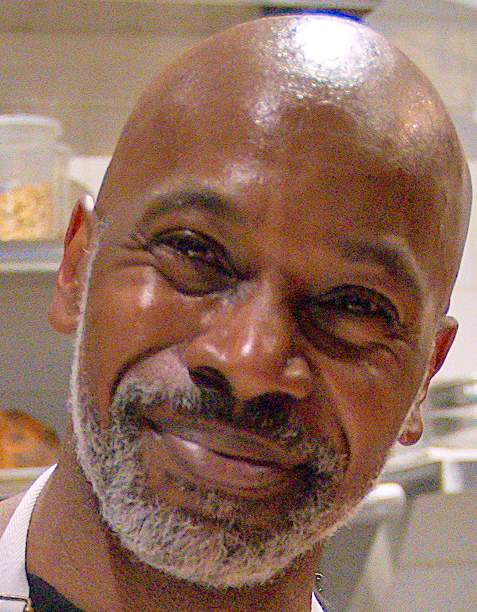 A bald, gray-bearded man giving a kind, humble smile