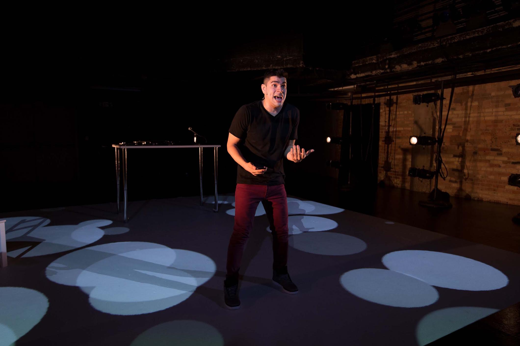 standing amid pools of light, Brian Quijada gestures energetically while speaking