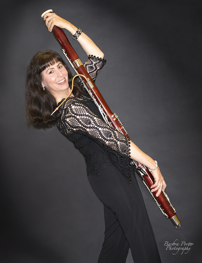 bassoonist in dynamic pose with bassoon smiling at the camera