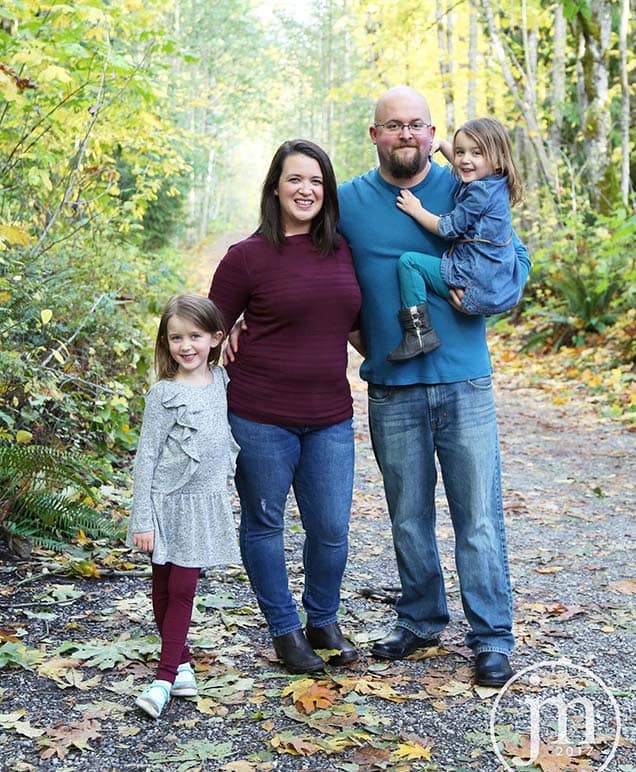 a family with two young children pose in a wooded area