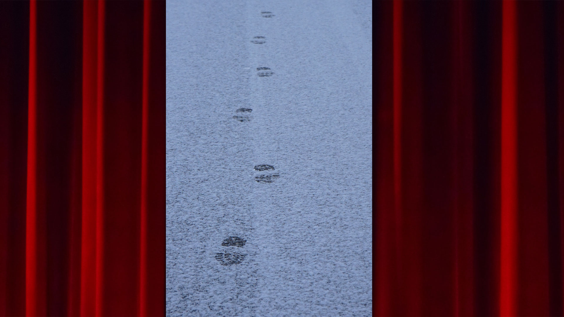 footprints on a snowy road appears between theatre curtains