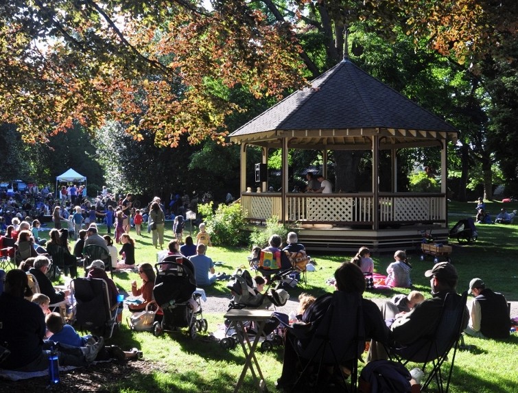 People seated on the grass and folding chairs watch a performance in front of a gazebo.