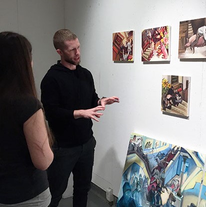 Two people discussing paintings displayed on a wall