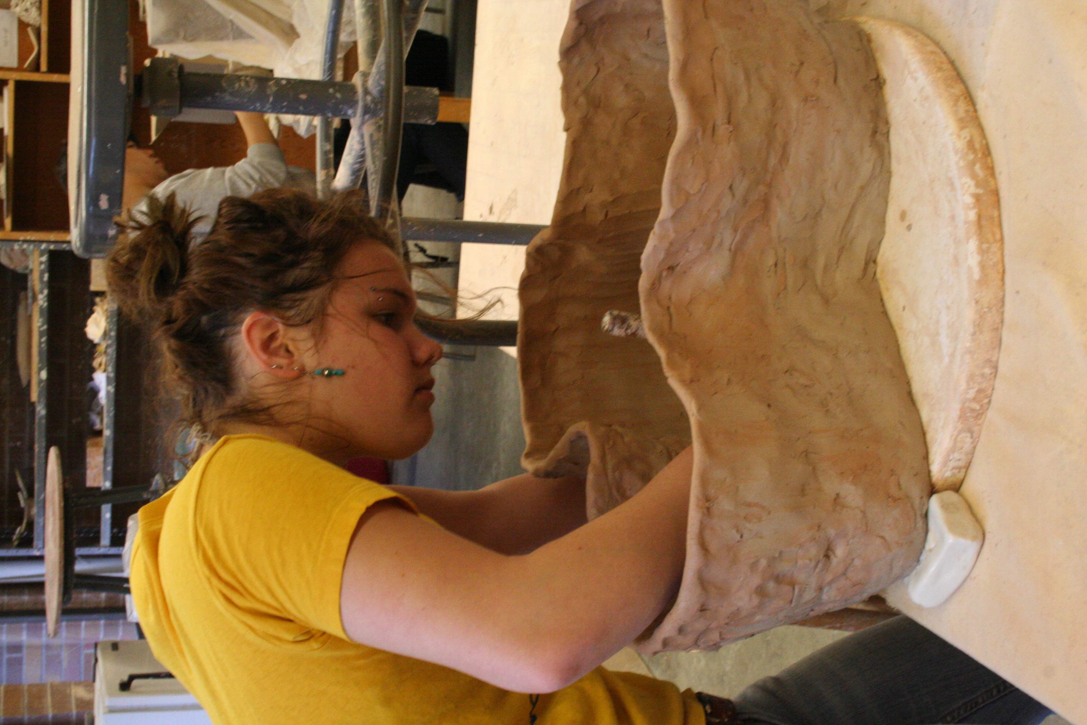 a student bends over and works on the inside of a large clay container