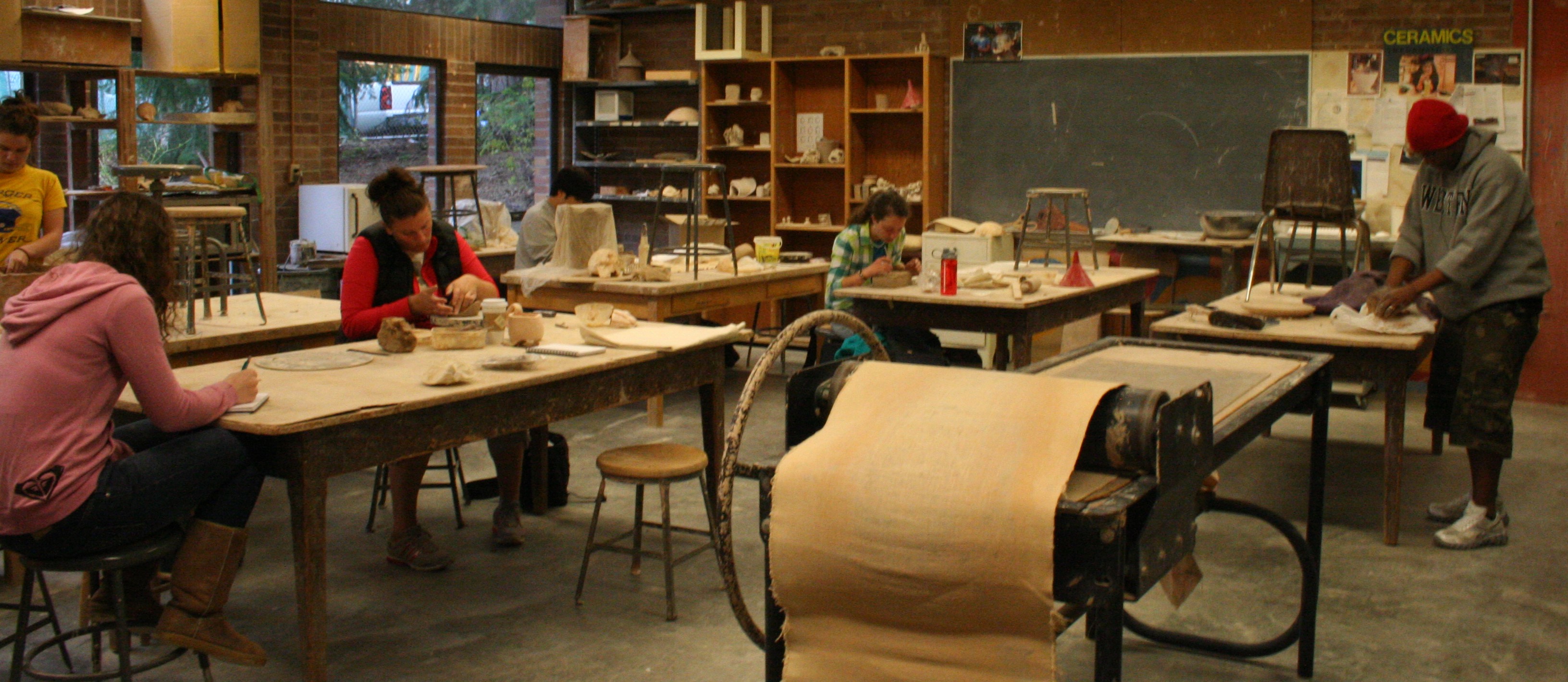 students working individually on clay projects at tables in a well-used studio space