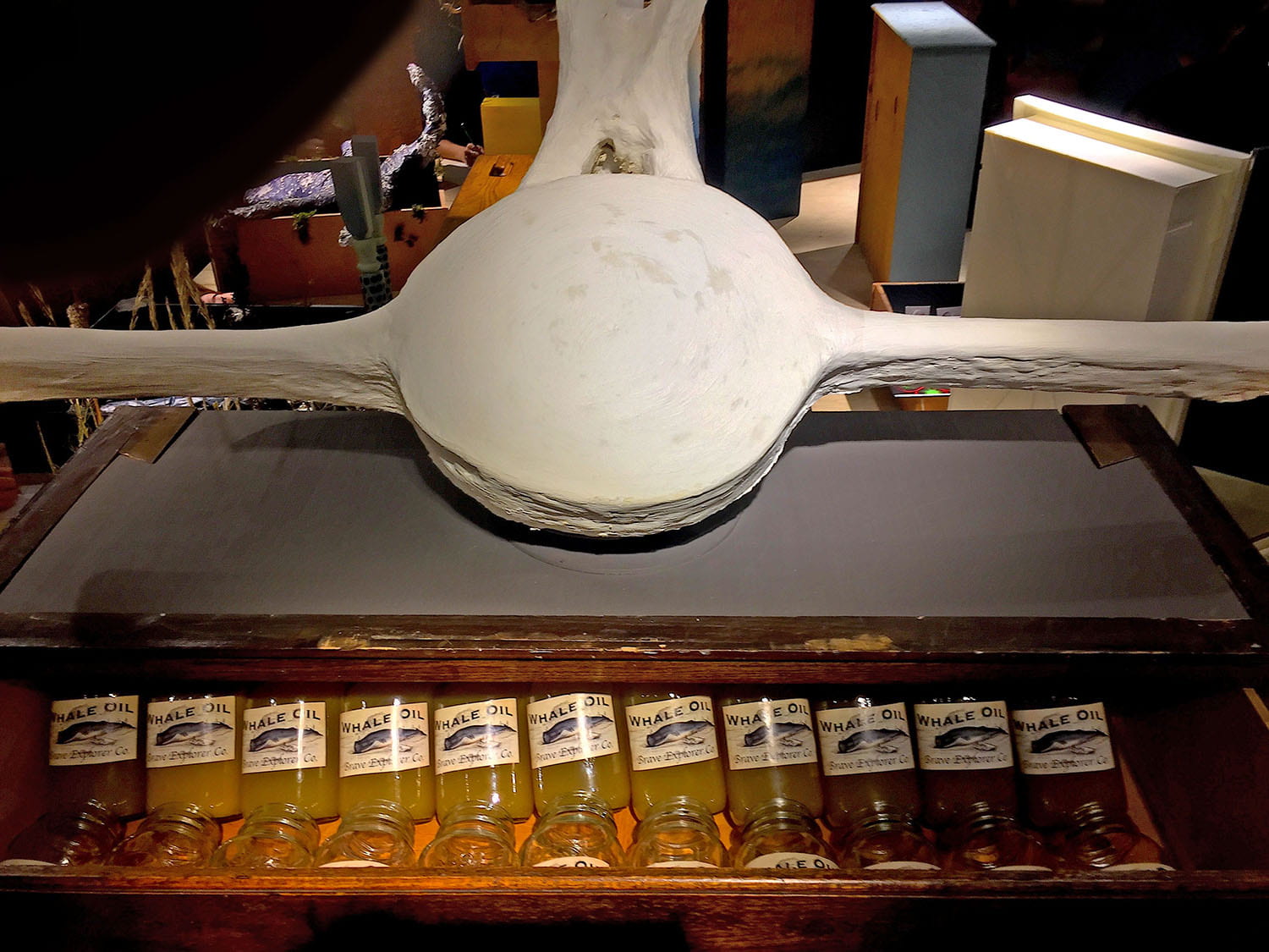 A table containing a round ceramic structure with long arms. Below it, an open drawer displays several jars of whale oil