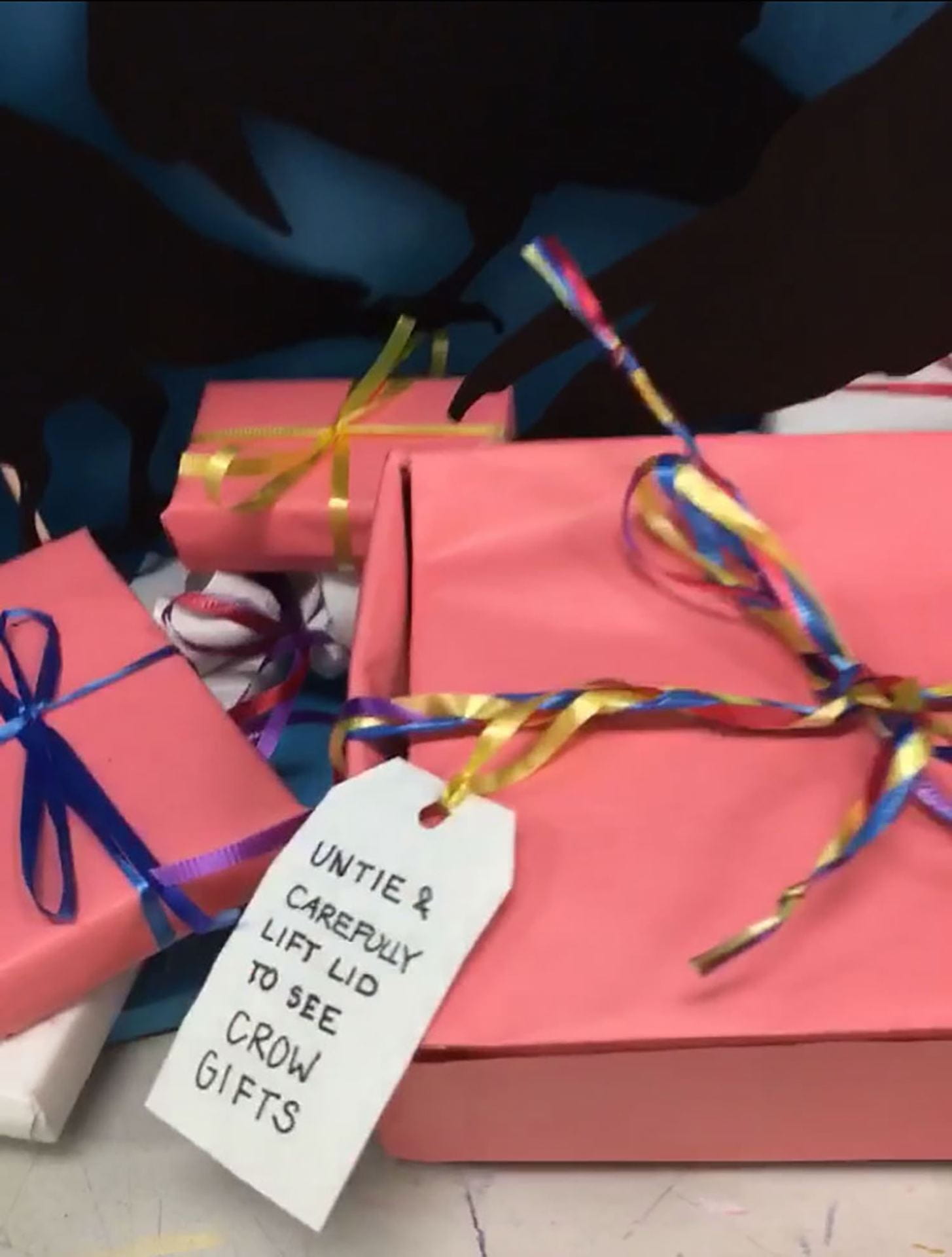 close-up of gift boxes with a tag labeled "untie & carefully lift lid to see crow gifts"