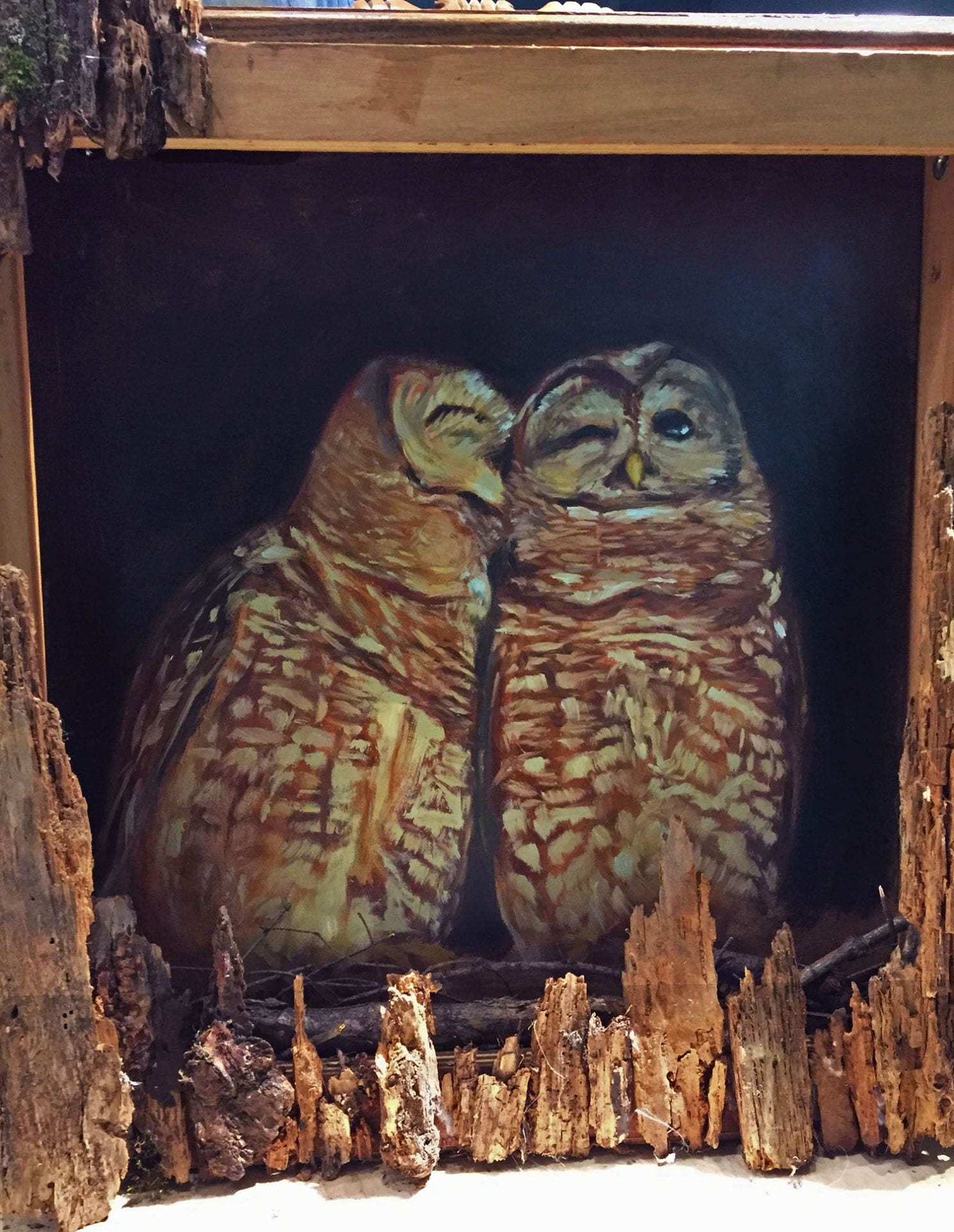 painting of two owls cuddling, framed with rotten chunks of tree.