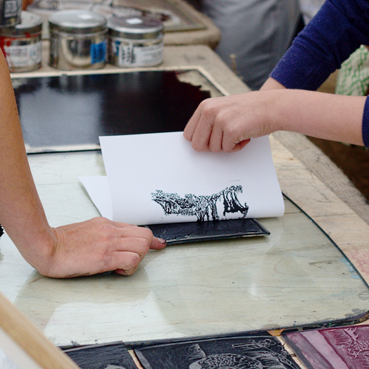 printmaking students peel a print off a cut block in the print lab
