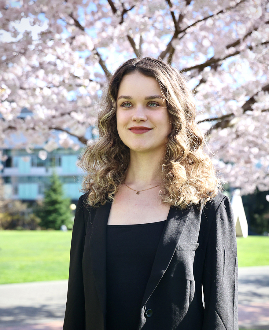 Cailey Peretti, dressed formally, standing in front of a blooming cherry blossom tree, smiling