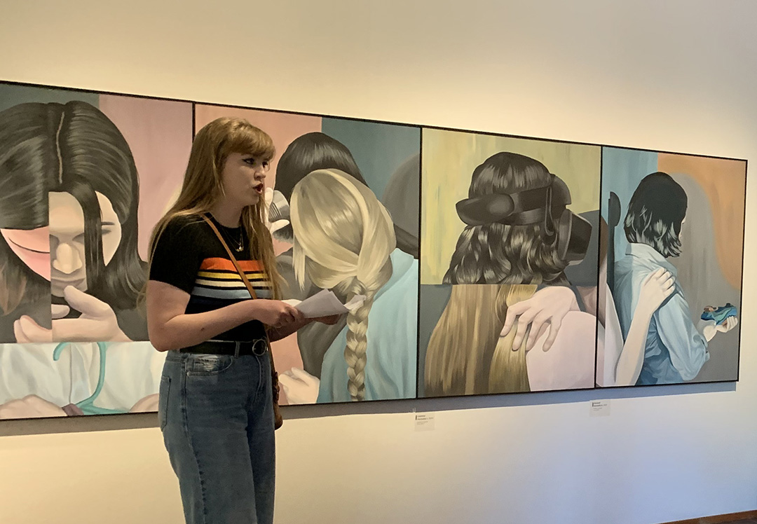 a person speaking in front of a row of painted portraits