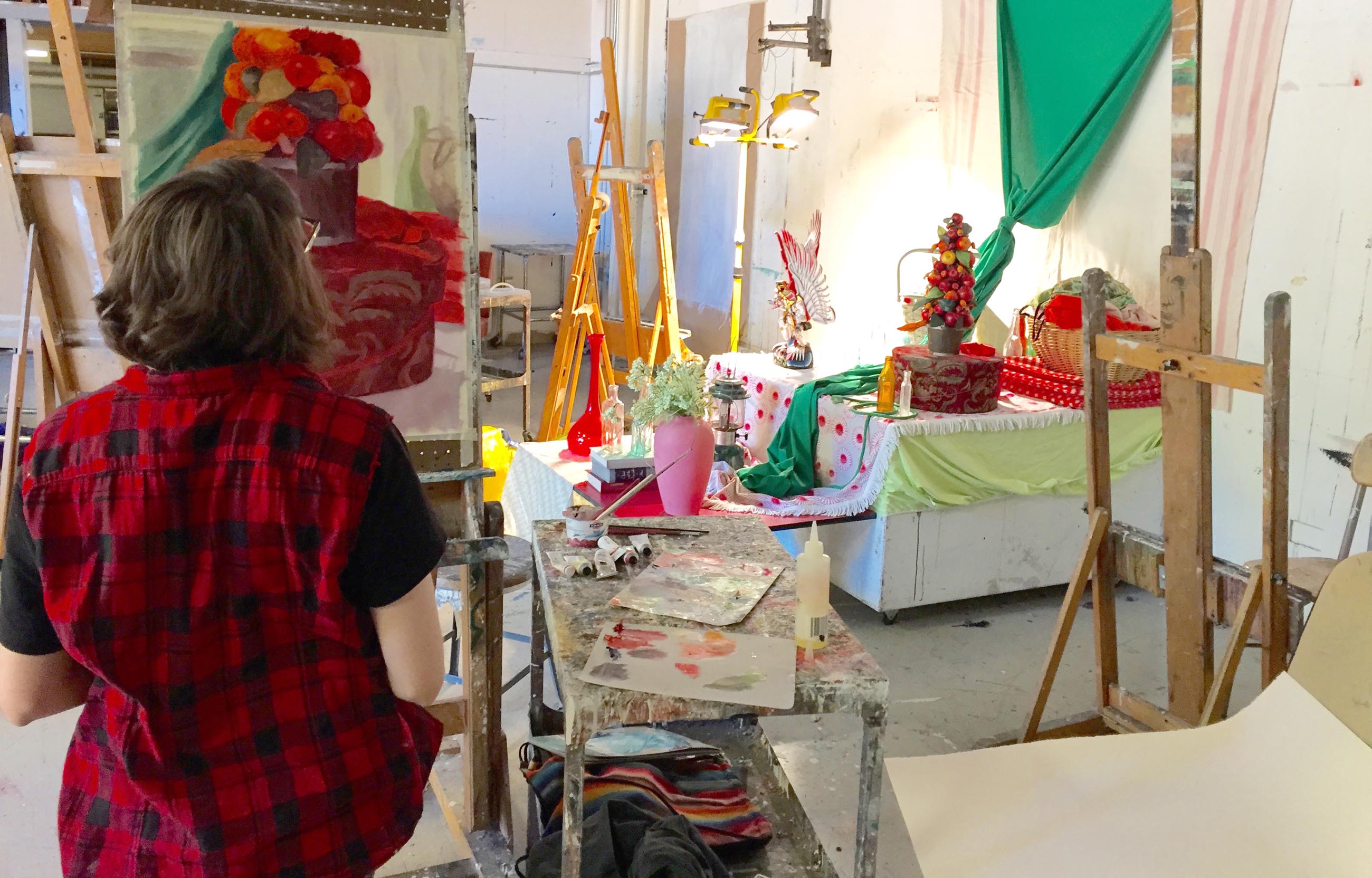 Student at an easel painting a colorful still life in a bright studio