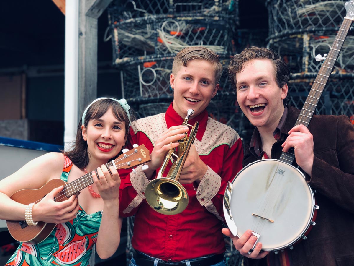 three cheerful actors, one holds a trumpet, one a banjo