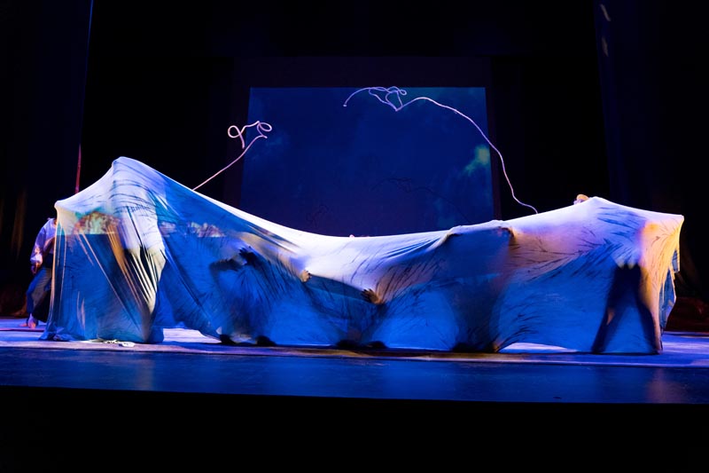 performers draped in diaphonous fabric in deep blue light 