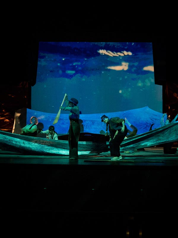 a stage scene of actors who seem to be paddling a boat at night.