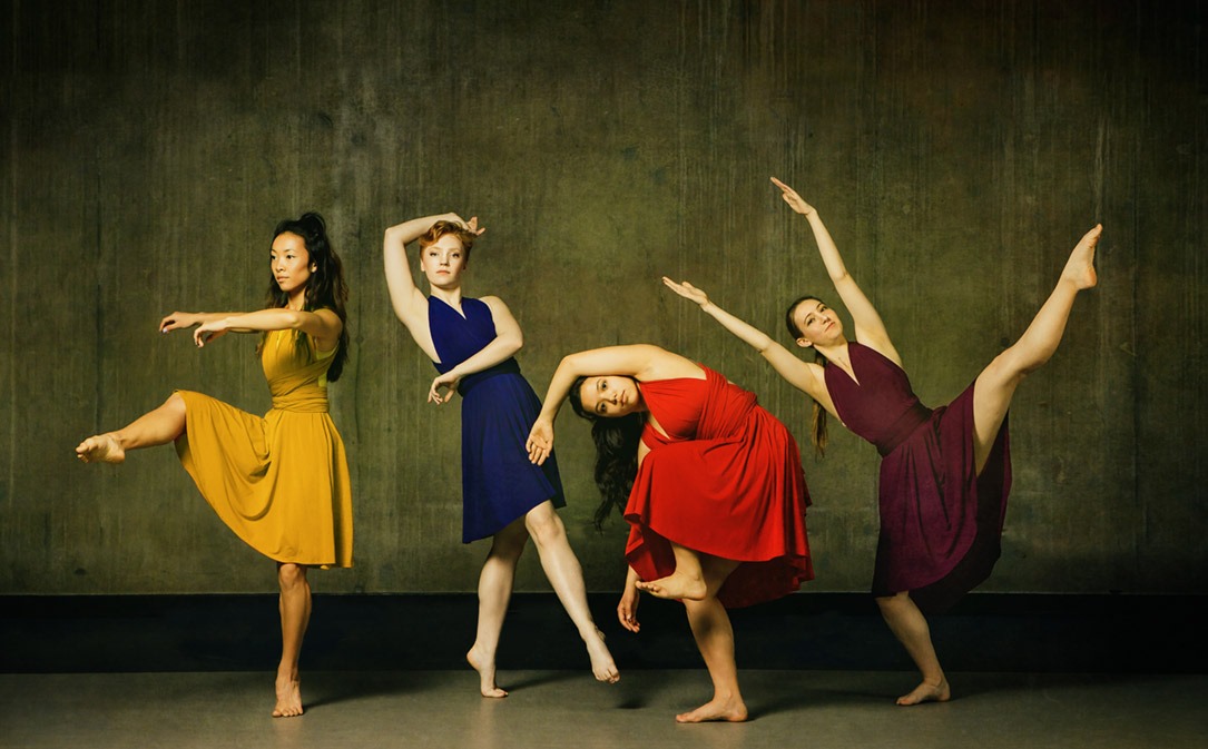 four dancers in solid color costumes pose dynamically