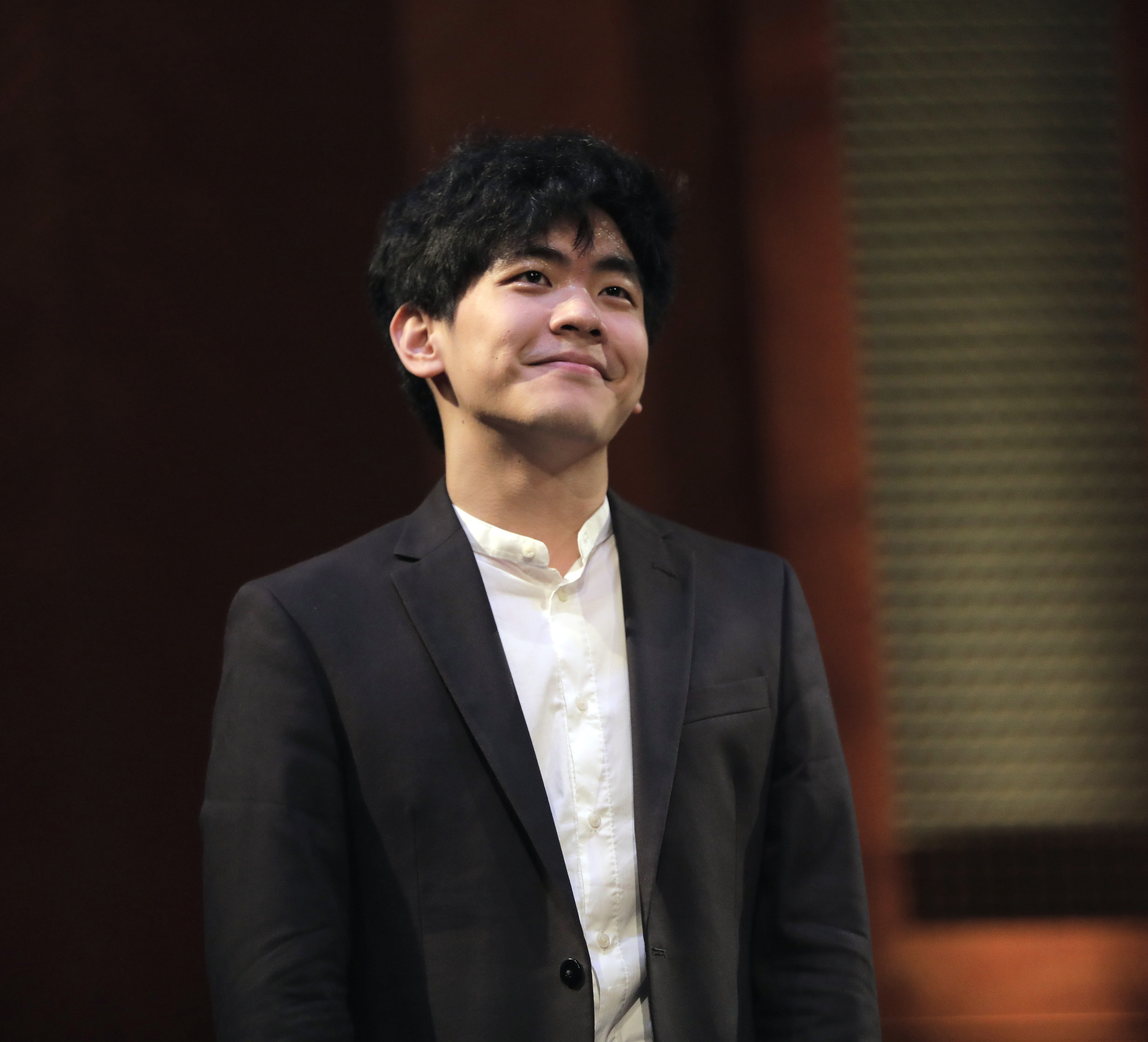 Pianist Daniel Hsu gazing up and afar with a happy closed-mouth smile