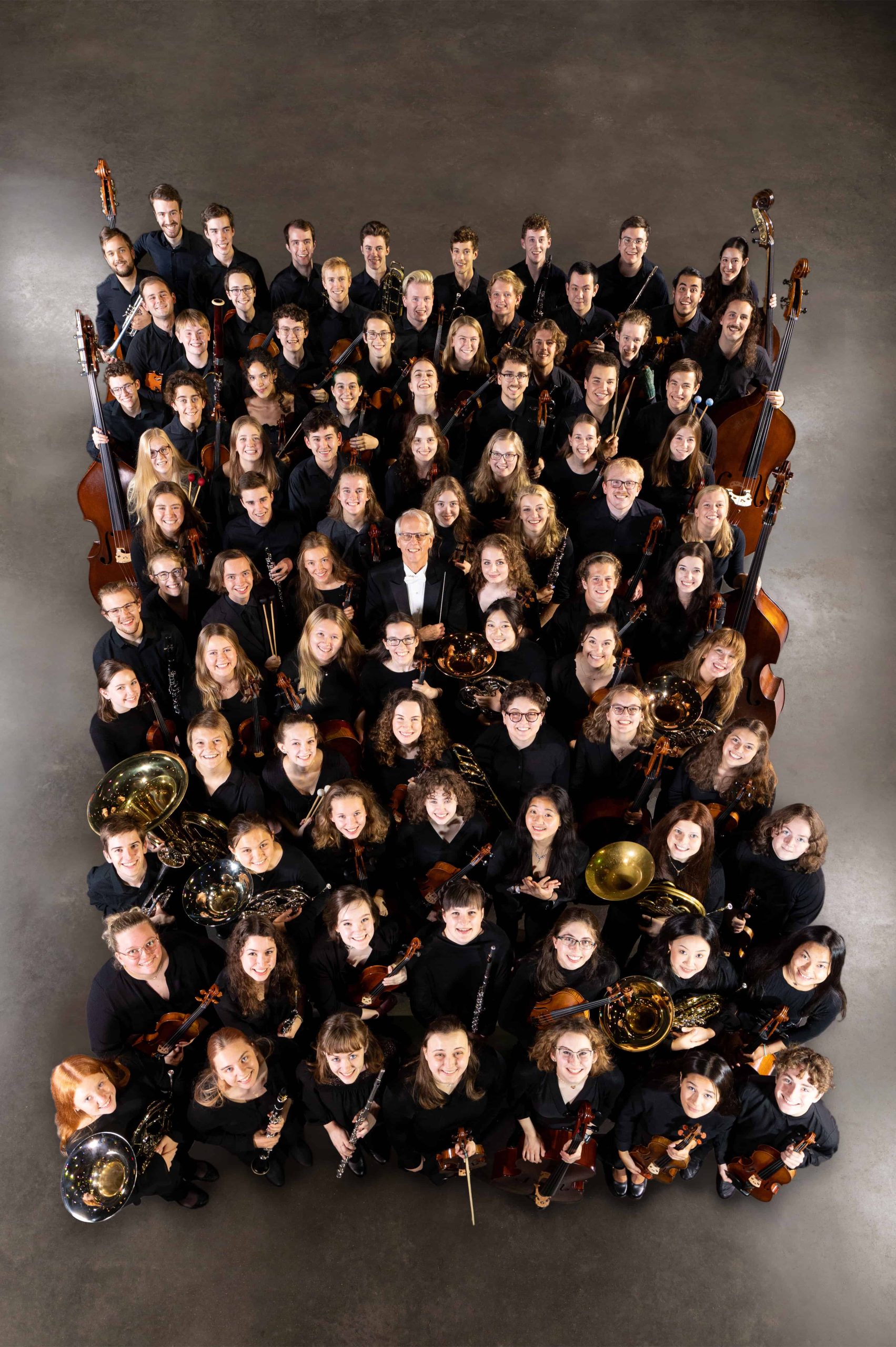 View from above: Members of an orchestra gathered together, looking up, smiling