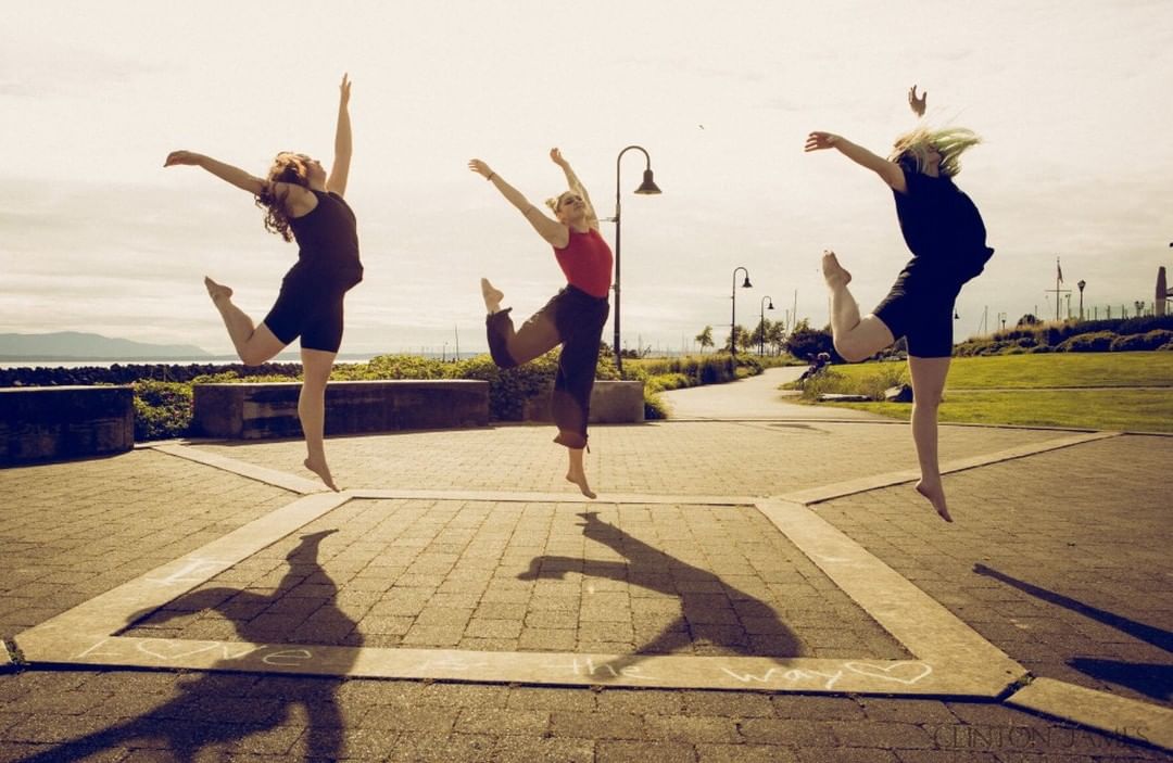 three dancers in the sun leap on a brick plaza